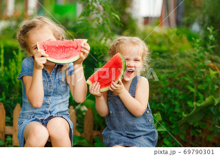 Little girls sit on watermelon and keep pieces  69790301