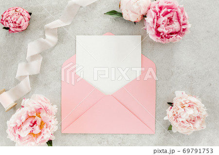 Mockup invitation, blank paper greeting card, pink envelope and peonies on gray stone table. Flower background. Flat lay, top view. 69791753