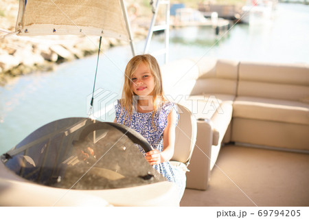 kid girl at helm of boat on pier. travel on water. 69794205
