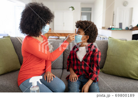 Mother putting face mask on her son at home Mother putting face mask on her son at home 69800189