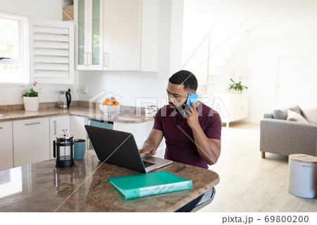 Man talking on smartphone while using laptop at home 69800200