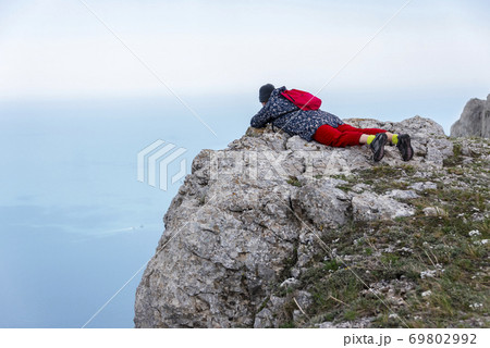 Girl lying on the edge of the mountain looks into the abyss against the background of clouds and sea 69802992