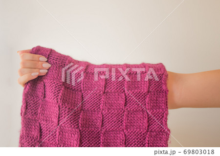 Knitted raspberry purple scarf in the hand of a young slender woman with a beautiful maicure. Knitted product close up mock up with copy space. Warm winter accessory Knitted raspberry purple scarf in the hand of a young slender woman with a beautiful maicure. Knitted product close up mock up with copy space. Warm winter accessory 69803018