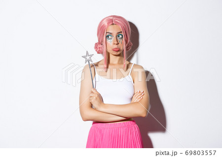Image of indecisive pouting girl in fairy costume, holding magic wand, looking thoughtful and standing over white background Image of indecisive pouting girl in fairy costume, holding magic wand, looking thoughtful and standing over white background 69803557