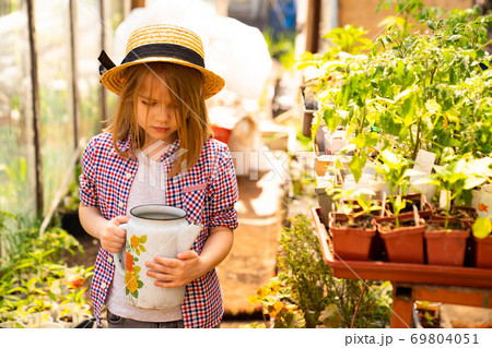 Adorable small girl kid in hat watering seedlings Adorable small girl kid in hat watering seedlings 69804051