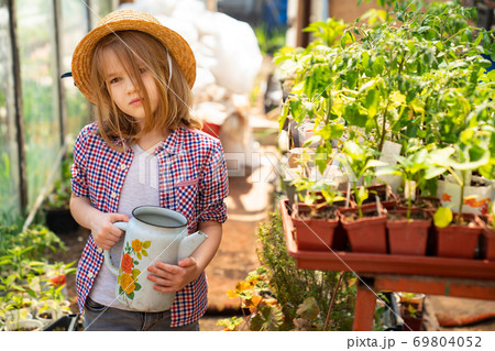 Adorable small girl kid in hat watering seedlings Adorable small girl kid in hat watering seedlings 69804052