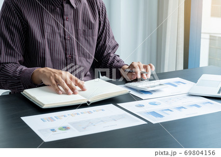 The hands of a male businessman are analyzing and calculating the annual income and expenses in a financial graph that shows results To summarize balances overall in office 69804156