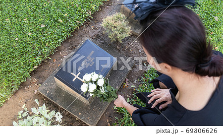 Mourning young woman laying white flowers on her family grave in beautiful green cemetery. 69806626