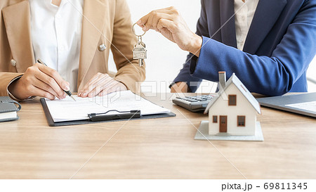 Estate agent holding a key and asking costumer for contract to buy, get insurance or loan estate. 69811345