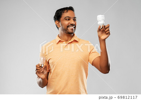 smiling indian man comparing different light bulbs smiling indian man comparing different light bulbs 69812117