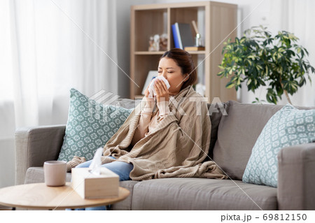 sick asian woman blowing nose with tissue at home 69812150