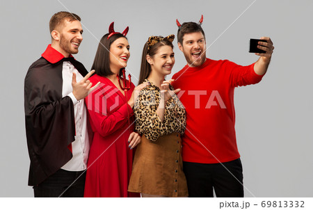 happy friends in halloween costumes taking selfie 69813332