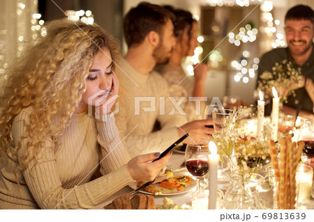 woman with smartphone at dinner party with friends 69813639