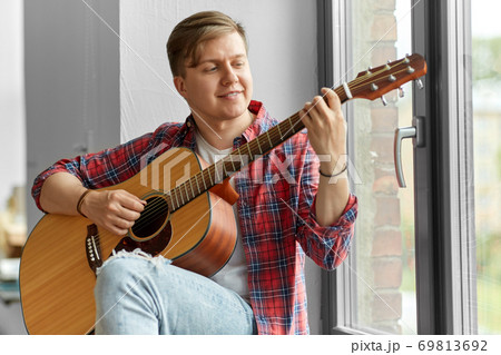 young man playing guitar sitting on windowsill 69813692