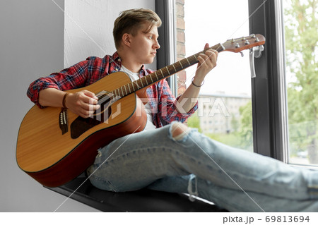 young man playing guitar sitting on windowsill 69813694