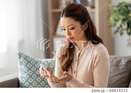 asian woman with glucometer makes blood sugar test 69814253