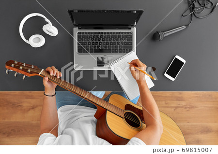 man with guitar writing to music book at table 69815007