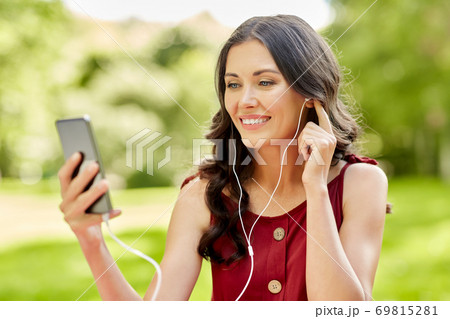 woman with smartphone and earphones at park 69815281