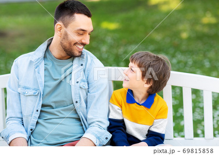 father with son sitting on park bench and talking 69815858