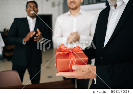 Close-up of hands of unrecognizable mature man holding red gift box tied to bow. 69817033