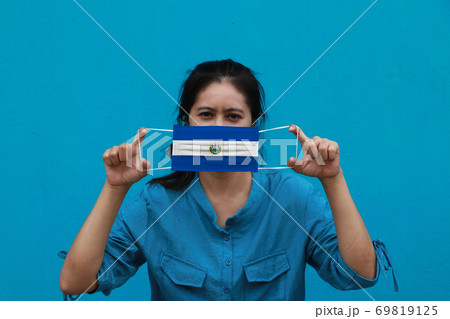 A woman and hygienic mask with El Salvador flag pattern in her hand and raises it to cover her face A woman and hygienic mask with El Salvador flag pattern in her hand and raises it to cover her face 69819125