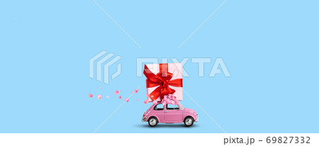 Pink car with gift box on a roof with flowers on a blue background. Pink car with gift box on a roof with flowers on a blue background. 69827332