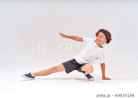 Having fun at training. Full length of a happy caucasian teenage boy in sportswear stretching legs and laughing while exercising isolated over grey background in studio Having fun at training. Full length of a happy caucasian teenage boy in sportswear stretching legs and laughing while exercising isolated over grey background in studio 69830166