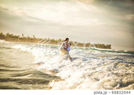 couple in white on sea beach in waves at sunset 69832044