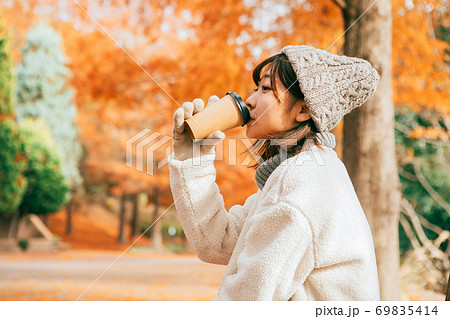 公園のベンチに座ってホットドリンクを飲む女性 公園のベンチに座ってホットドリンクを飲む女性 69835414