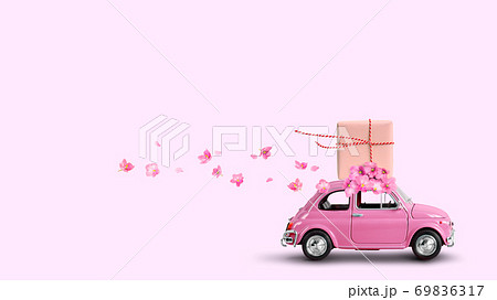 Pink car with gift box on a roof with flowers on pink background. 69836317