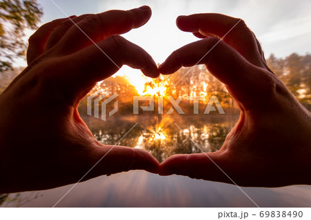 Male hands making a heart-shaped gesture against the background of sunset or sunrise on a river or lake. 69838490