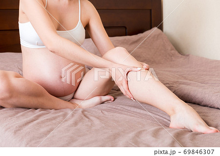 Pretty pregnant woman hands massaging leg sitting on bed Pretty pregnant woman hands massaging leg sitting on bed 69846307