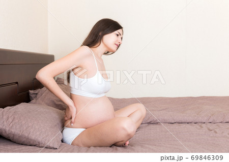 beautiful pregnant woman touching her tummy and keeping one hand on her back at home on bed beautiful pregnant woman touching her tummy and keeping one hand on her back at home on bed 69846309
