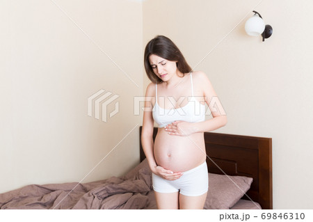 Young pretty pregnant woman, in pain, sitting on bed in bedroom, preparing to give a birth Young pretty pregnant woman, in pain, sitting on bed in bedroom, preparing to give a birth 69846310