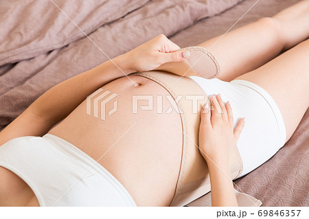 closeup pregnant woman dresses bandage on belly at home on bed. Orthopedic abdominal support belt closeup pregnant woman dresses bandage on belly at home on bed. Orthopedic abdominal support belt 69846357