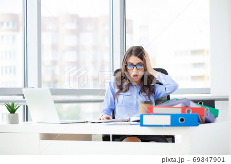 Young office worker sitting at desk holding head because of pain in office Young office worker sitting at desk holding head because of pain in office 69847901