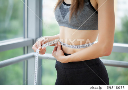 A slender woman measures the size of her waist. A slender woman measures the size of her waist. 69848033