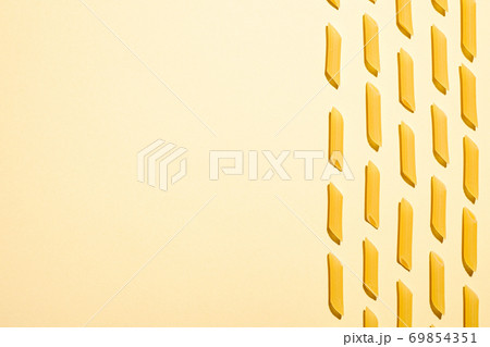 Italian pasta, raw penne tube macaroni pattern on yellow cream background, top view copy space, abstract food Italian pasta, raw penne tube macaroni pattern on yellow cream background, top view copy space, abstract food 69854351