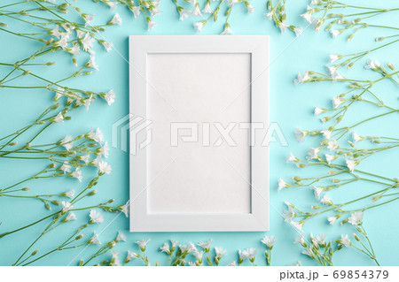 White empty photo frame mockup with mouse-ear chickweed flowers on blue background, top view copy space 69854379