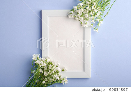 White empty photo frame mockup with mouse-ear chickweed flowers on blue background, top view copy space 69854397