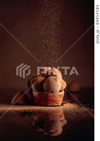 Chocolate truffles in small wooden dish sprinkled with cocoa powder. Black reflective background. 69854584