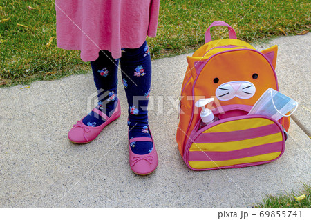 A little girl shoes next to a school bag with a face mask and hand sanitizer A little girl shoes next to a school bag with a face mask and hand sanitizer 69855741
