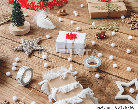 Christmas presents wrapped in craft paper with white fluffy pompons and fringe as decoration. Wooden table with hand made New Year gifts for children with toy ship and train. 69856766