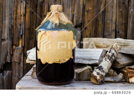 Craft alcohol birch tincture in a large glass bottle on a wooden table, Russian folk recipe Craft alcohol birch tincture in a large glass bottle on a wooden table, Russian folk recipe 69863029