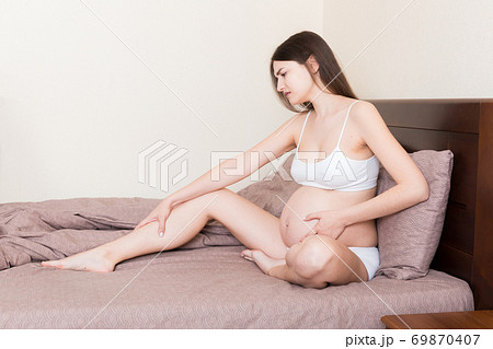 Pretty pregnant woman hands massaging leg sitting on bed Pretty pregnant woman hands massaging leg sitting on bed 69870407