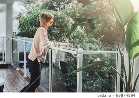 Middle-aged woman enjoying the tropical view from the balcony Middle-aged woman enjoying the tropical view from the balcony 69874994