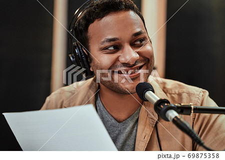 Close up portrait of happy young male radio host in headphones smiling aside while talking, broadcasting in studio 69875358