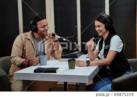 Portait of two happy radio hosts, man and woman smiling while talking with each other, moderating a live show in studio Portait of two happy radio hosts, man and woman smiling while talking with each other, moderating a live show in studio 69875359