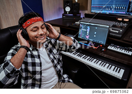 Young man, male artist in headphones sitting with eyes closed while listening to music in recording studio 69875362