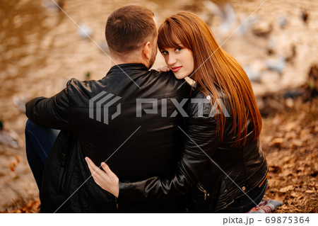 couple sitting on Bank of river in autumn park. 69875364